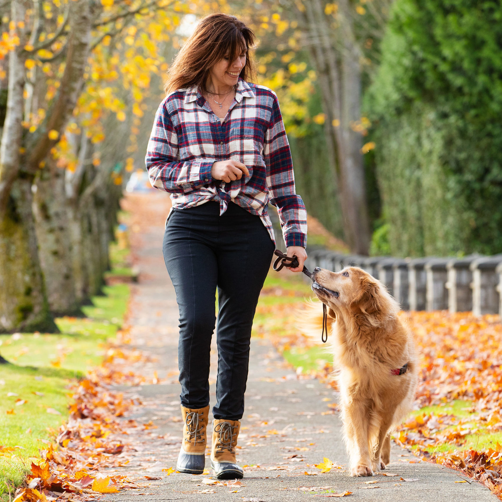 Woman walking golden retriever dog in Fall leaves