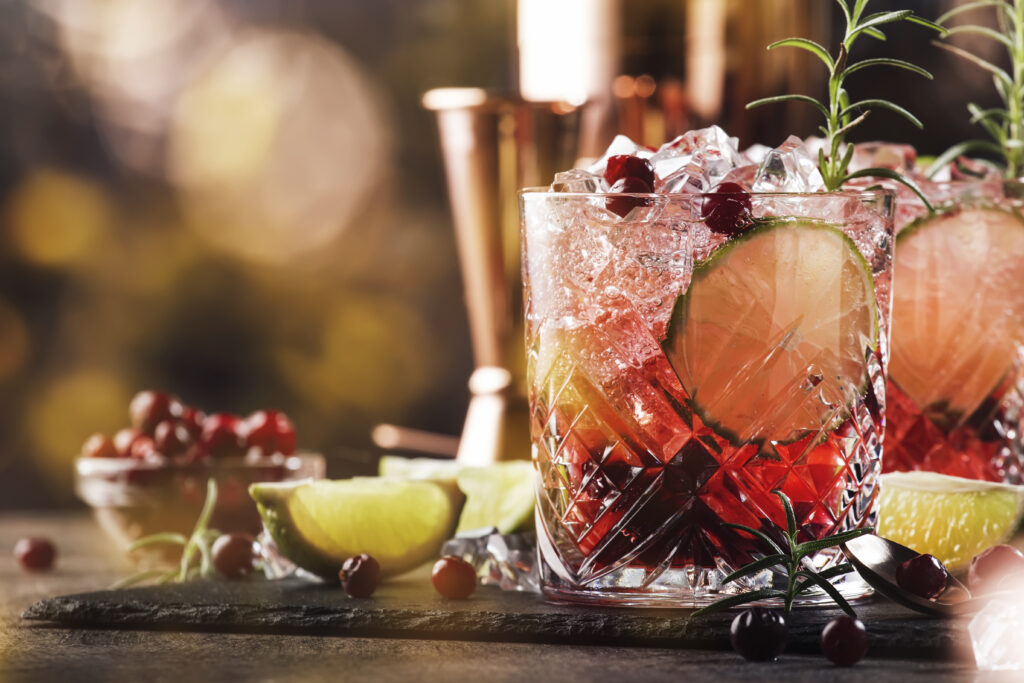 Red alcohol cocktail with cranberries, ice and rosemary on woode